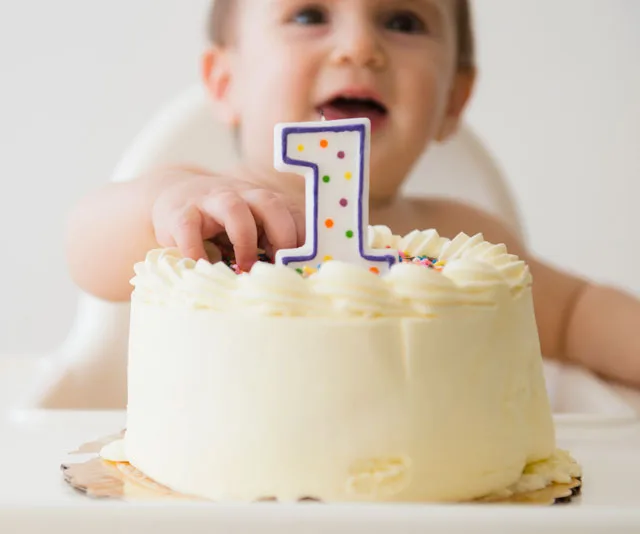Toddler celebrating first birthday with a cake and a candle shaped as the number one.