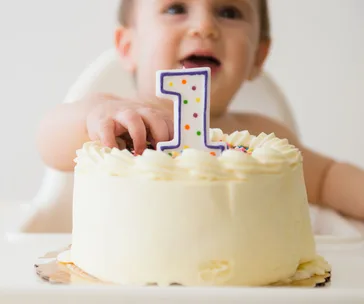 Toddler celebrating first birthday with a cake and a candle shaped as the number one.