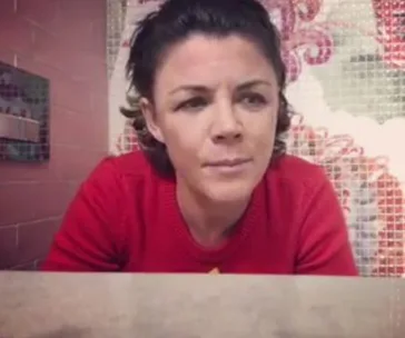 Woman in a red sweater looking thoughtfully, against a mosaic-tiled background.