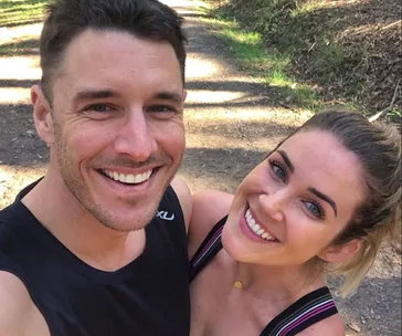A smiling couple taking a selfie on a sunny outdoor trail.