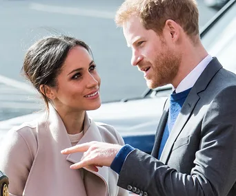 Two people engaged in conversation outdoors, one gesturing with a hand, both appearing attentive and engaged.
