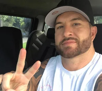 Man in a cap making a peace sign while seated in a car.