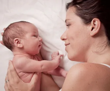 A mother lovingly holding and gazing at her newborn baby on a white bed.
