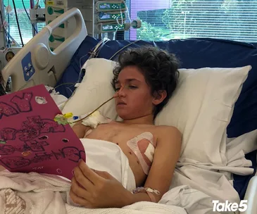 Young boy in hospital bed, holding a handmade card, medical equipment surrounding him.