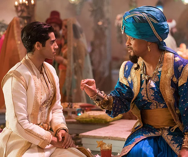 Aladdin and Genie in vibrant attire at a lively gathering, engaged in a conversation.