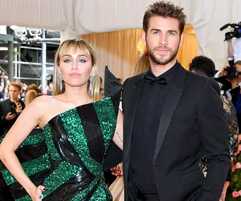 Two individuals in formal attire at an event, with one in a green dress and the other in a black suit.