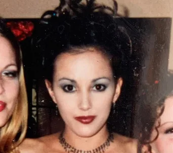 Formal photo of a woman with dark updo and bold makeup, wearing a necklace.