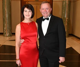 A couple dressed formally, the woman in a red dress and the man in a black tuxedo, smiling and posing indoors.