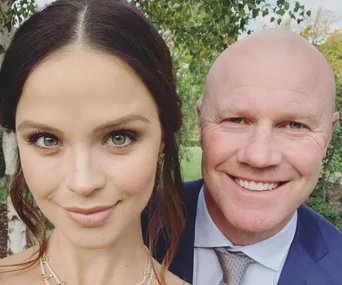 Man and woman smiling outdoors, woman with dark hair, dressed elegantly.