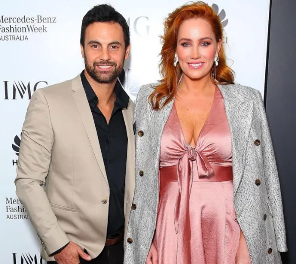 Man in beige blazer and woman in pink dress with gray coat, posing at a fashion event.