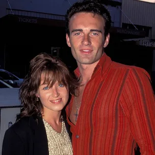 A couple posing closely outdoors, with the woman wearing a sparkly top and the man in a red striped shirt.