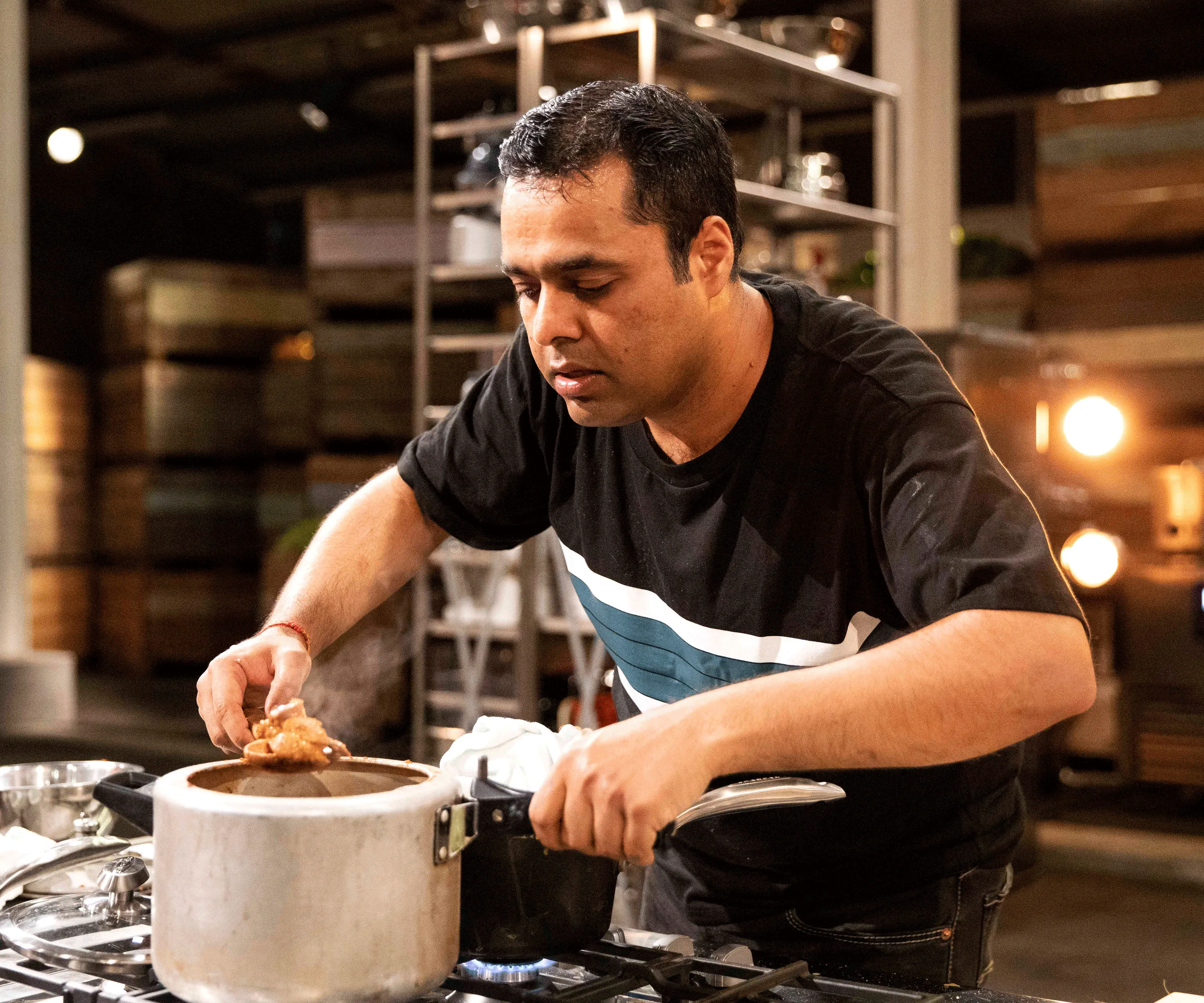 A man cooking intently using a pot on a stove in a kitchen setting.