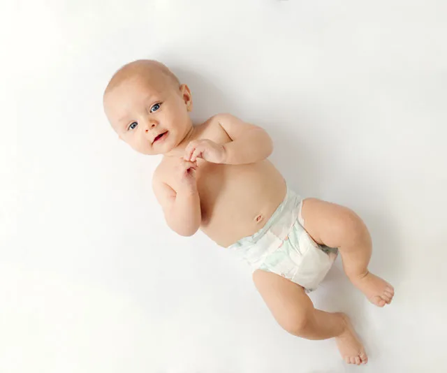 Baby lying on a white surface, wearing a diaper.