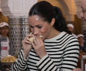 Woman in a striped sweater eating bread in a Moroccan-style interior.