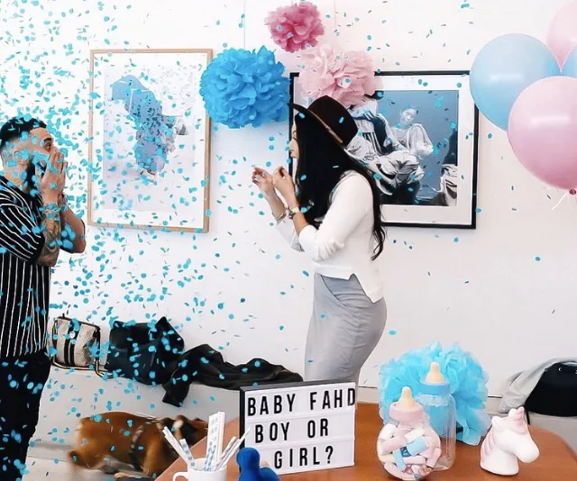 "Gender reveal party with blue confetti and balloons; sign reads 'Baby Fahd Boy or Girl?' amidst joyful celebration."