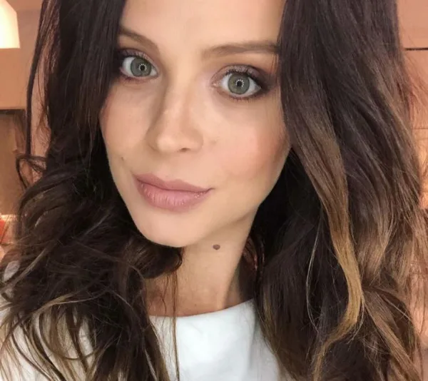 Young woman with long, dark hair and light eyes looking at camera with a neutral expression.