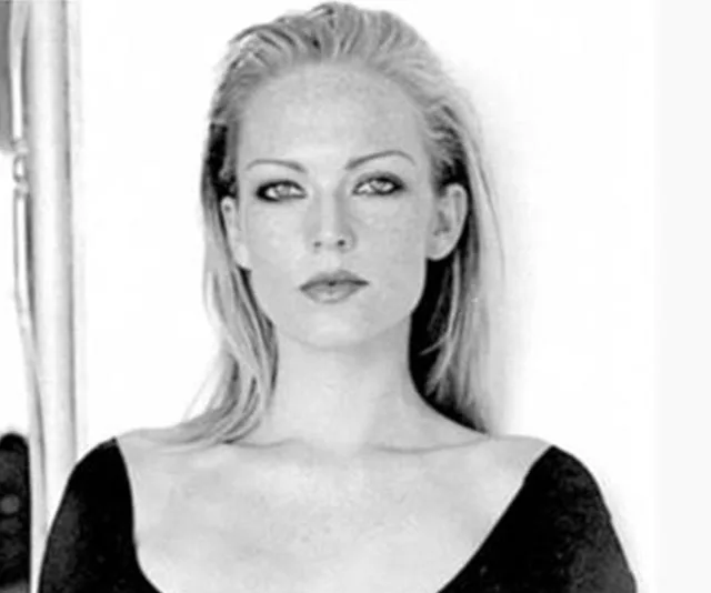A black-and-white photo of a woman with light hair and a serious expression, wearing a dark top.