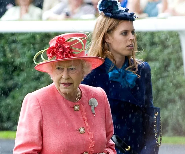A woman in a pink outfit and floral hat walks with another woman in a navy coat and hat in the rain.
