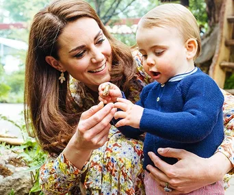 Princess holding her son, both smiling, in a garden setting.