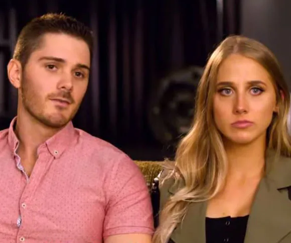 A couple sits together on a couch, both looking serious and contemplative.