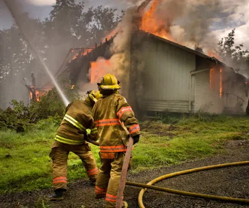 Firefighters battling a house fire, flames and smoke rising from the roof.