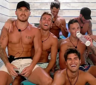 Group of six shirtless men on a patio, some laughing and one drinking water.