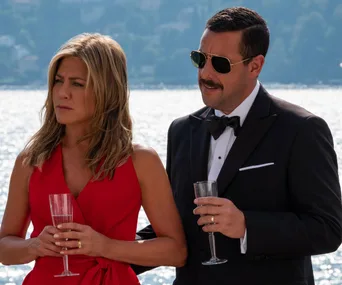 Two people in formal attire holding champagne glasses, standing by a body of water on a sunny day.