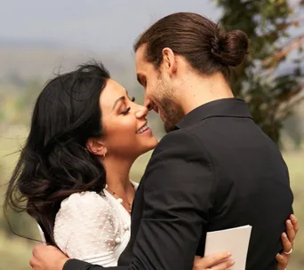 A couple embracing outdoors, smiling and gazing into each other's eyes lovingly.
