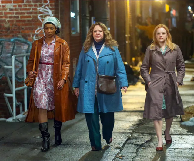 Three women in vintage coats walking down a dimly lit alley, exuding confidence and determination.