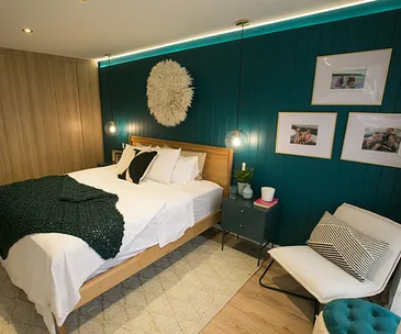 Bedroom with teal accent wall, modern decor, a wooden bed, white bedding, pendant lights, and framed photos on the wall.