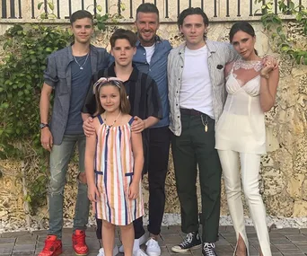 A family of six posing outdoors, including two men, two boys, one woman, and a young girl in a striped dress.