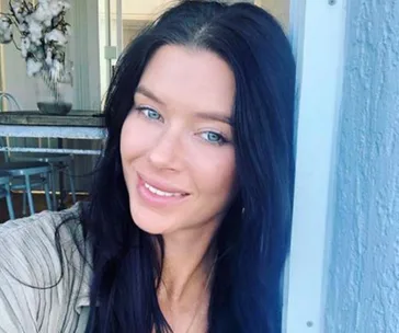 Black-haired woman smiling indoors, light-filled room in background.