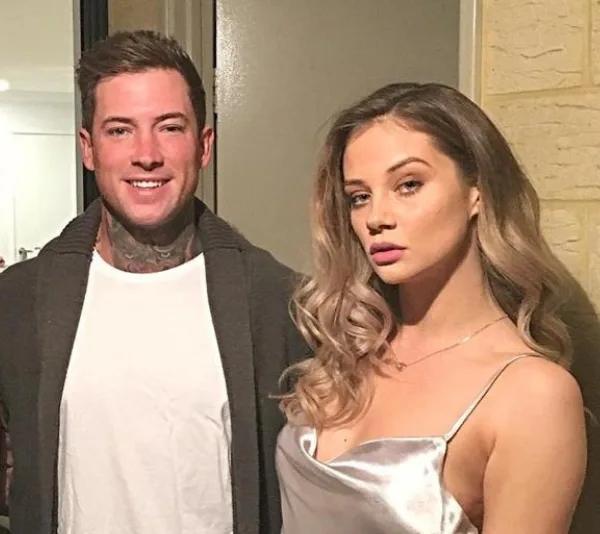 A man and a woman posing together indoors; woman in a silver dress, man in a dark sweater.