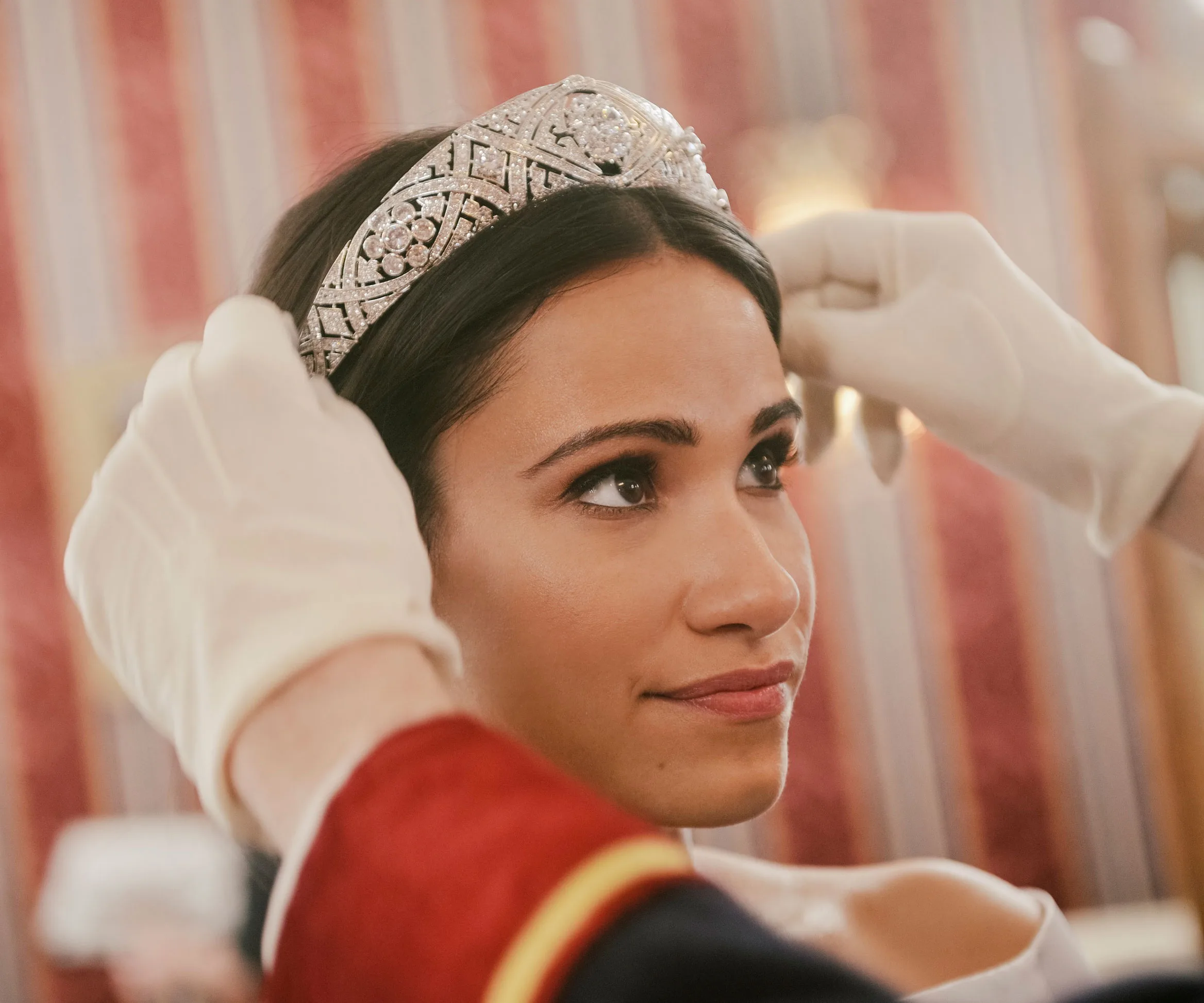 Actress Tiffany Smith as Meghan Markle in "Becoming Royal," wearing a tiara, with gloved hands adjusting it.