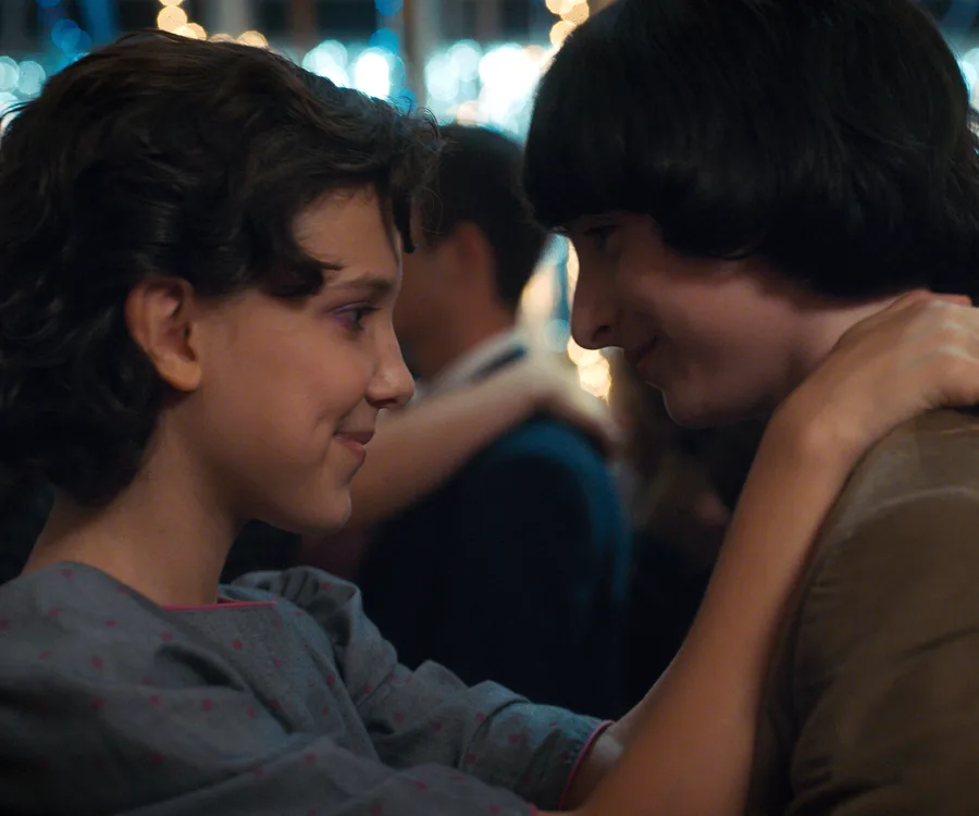 Two young characters smiling closely while dancing at a party with blurred lights in the background.