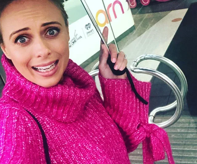 Person in a bright pink sweater making an expressive face, holding a handlebar indoors near a sign with "ARN" partly visible.