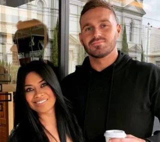 Couple posing and smiling outside a building, one holding a coffee cup.