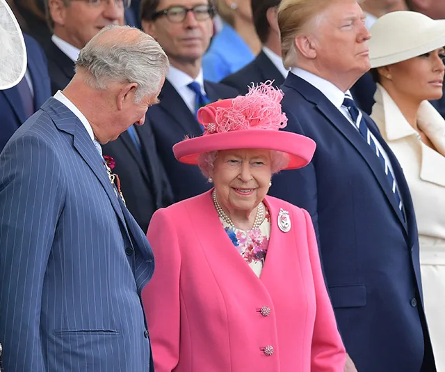 Group of dignitaries, including a woman in a bright pink outfit and hat, attending an outdoor event.