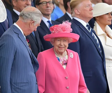 Group of dignitaries, including a woman in a bright pink outfit and hat, attending an outdoor event.