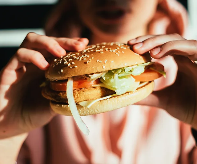 Person holding a sesame seed bun sandwich with lettuce, tomato, and a patty.