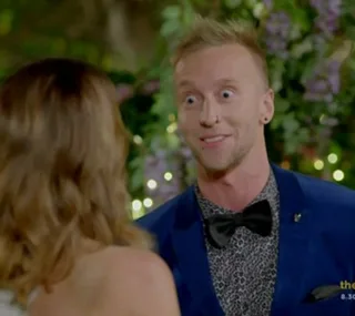 Man in a blue suit and bow tie talking to a woman with blurred background.
