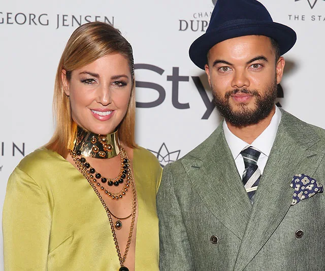 A woman in a yellow dress and a man in a green suit with a blue hat smiling at an event.