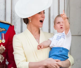A woman in a yellow dress holds a child pointing upward, both appear happy, with a soldier partially visible on the left.