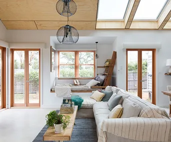 Bright, modern living room with corner windows, skylights, L-shaped sofa, and wooden accents.
