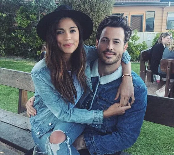 A couple sitting on a bench, with the woman wearing a hat and denim, embracing the man dressed in a denim jacket.