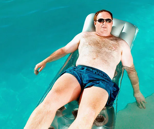 Man wearing sunglasses lounging on an inflatable raft in a swimming pool.