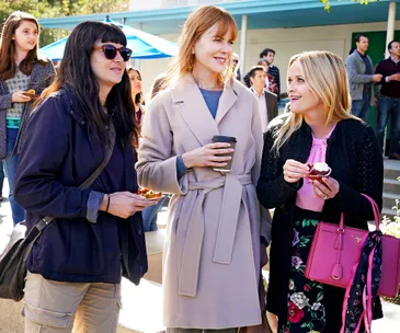 Three women at an outdoor gathering, one holding a coffee cup, another with sunglasses, and the third with a cupcake.