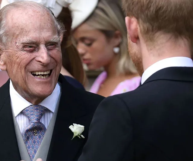 Elderly man in suit smiling at a younger man in a crowd, outdoors at a formal event.