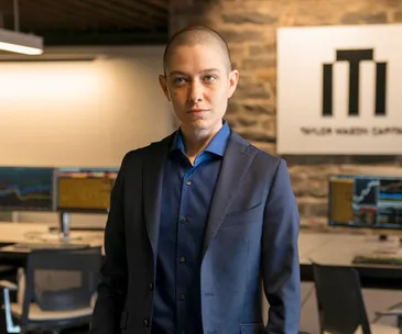 Taylor Mason from "Billions" stands in an office with trading screens in the background.