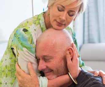 A comforting embrace between a woman and a bald man seated, conveying support and care.